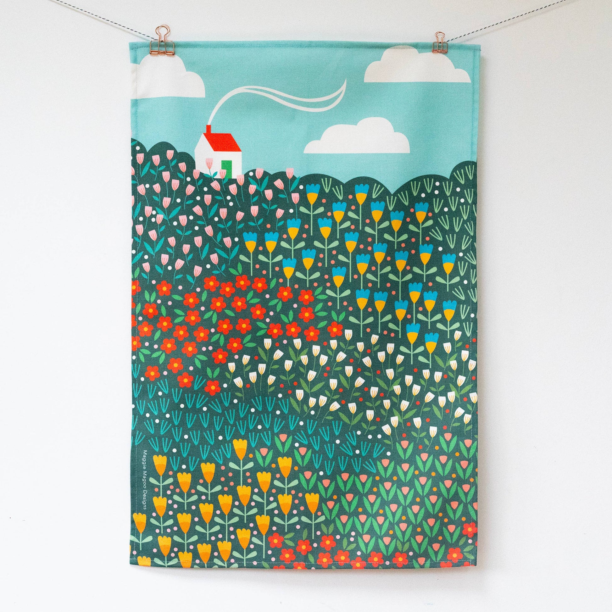 Hanging teatowel with a bright meadow design and a white house with red roof in the top left corner