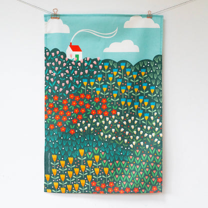 Hanging teatowel with a bright meadow design and a white house with red roof in the top left corner