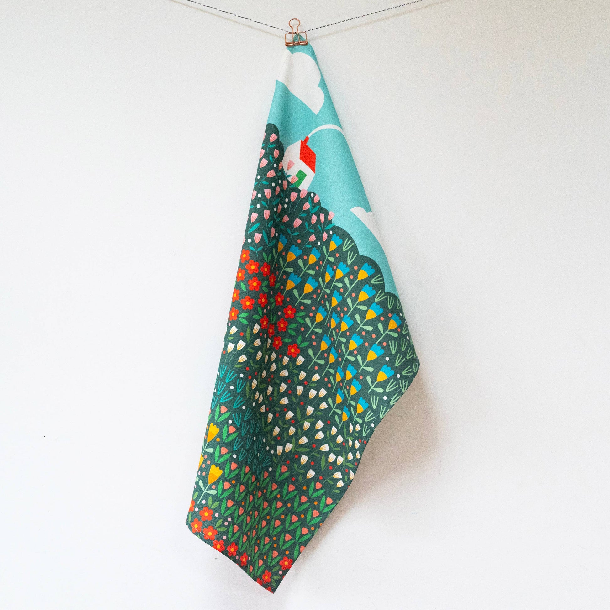 Hanging teatowel with a bright meadow design and a white house with red roof in the top left corner