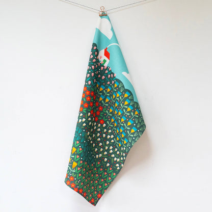 Hanging teatowel with a bright meadow design and a white house with red roof in the top left corner
