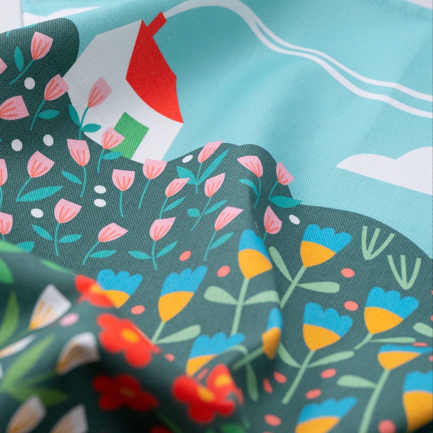 Teatowel with a bright meadow design and a white house with red roof in the top left corner