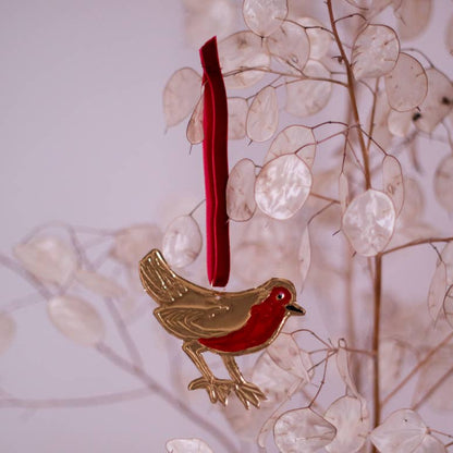 A handmade tin embossing tin ornament in the shape of a red robin with a pink tree in the background.