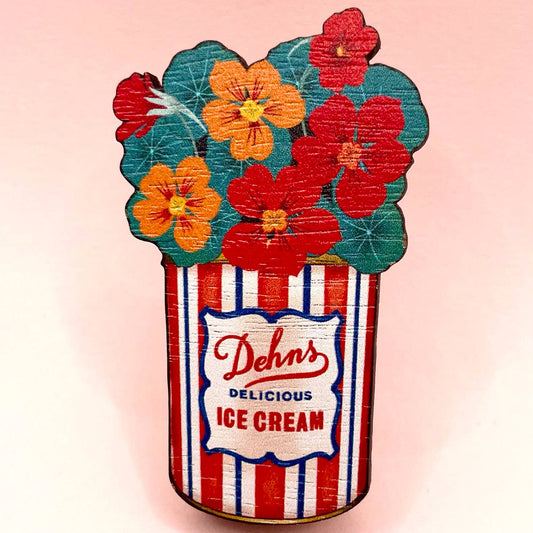 A wooden brooch pin shaped like a vintage ice cream tin with red and orange flowers, made from sustainable walnut.