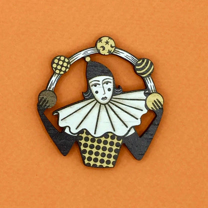 A wooden pin brooch depicting a vintage style circus juggler, with a sombre look, laser-cut from sustainable walnut wood.