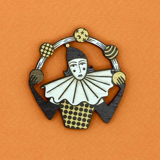 A wooden pin brooch depicting a vintage style circus juggler, with a sombre look, laser-cut from sustainable walnut wood.