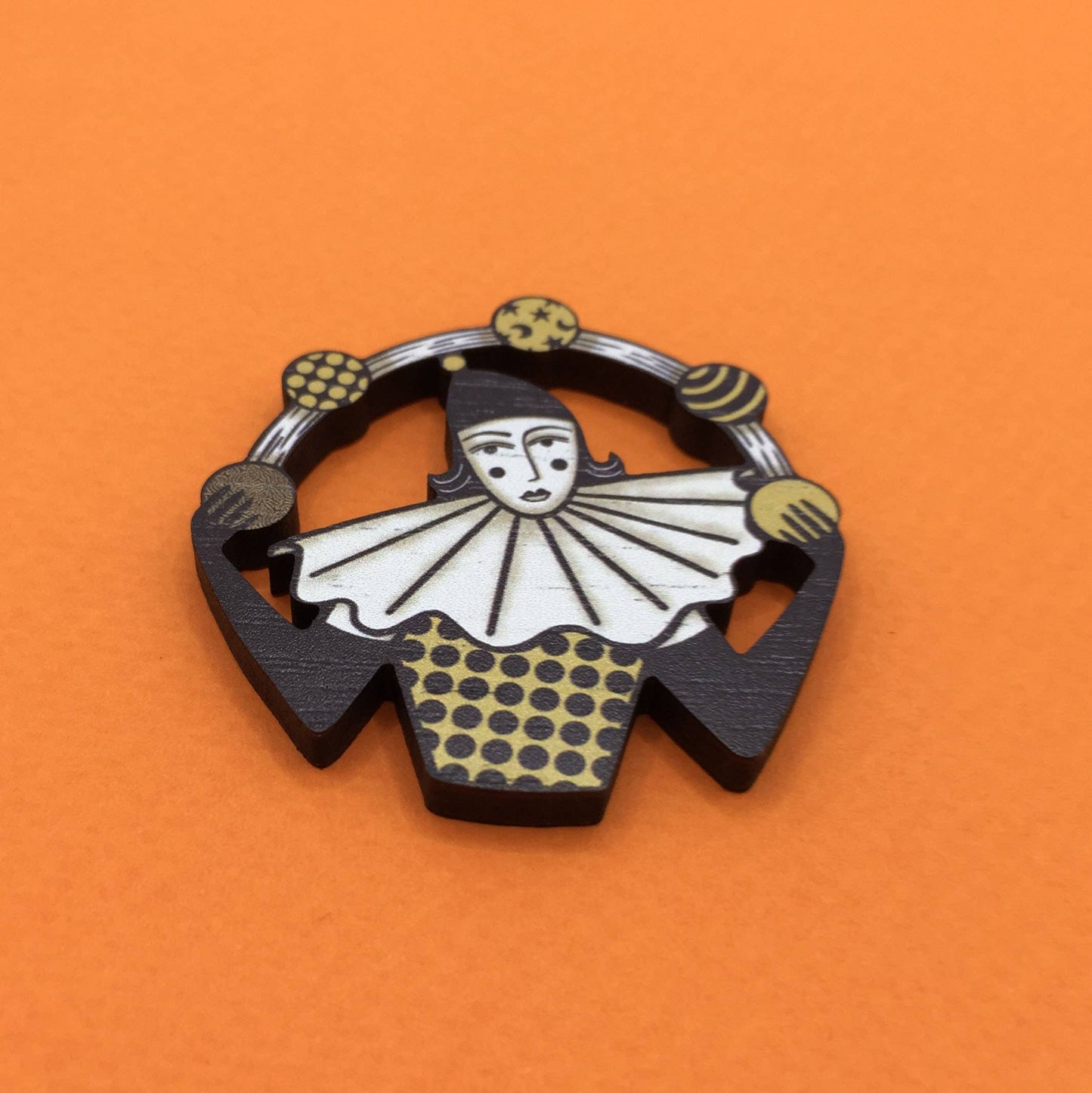 A wooden pin brooch depicting a vintage style circus juggler, with a sombre look, laser-cut from sustainable walnut wood.