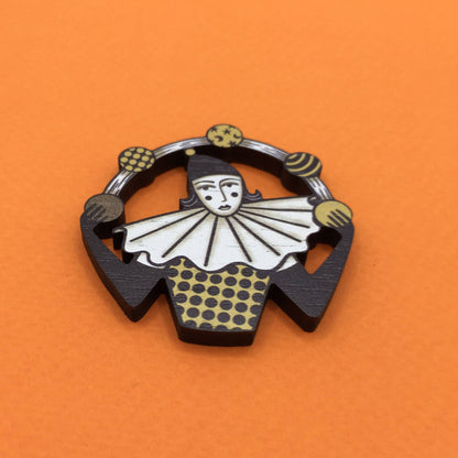 A wooden pin brooch depicting a vintage style circus juggler, with a sombre look, laser-cut from sustainable walnut wood.