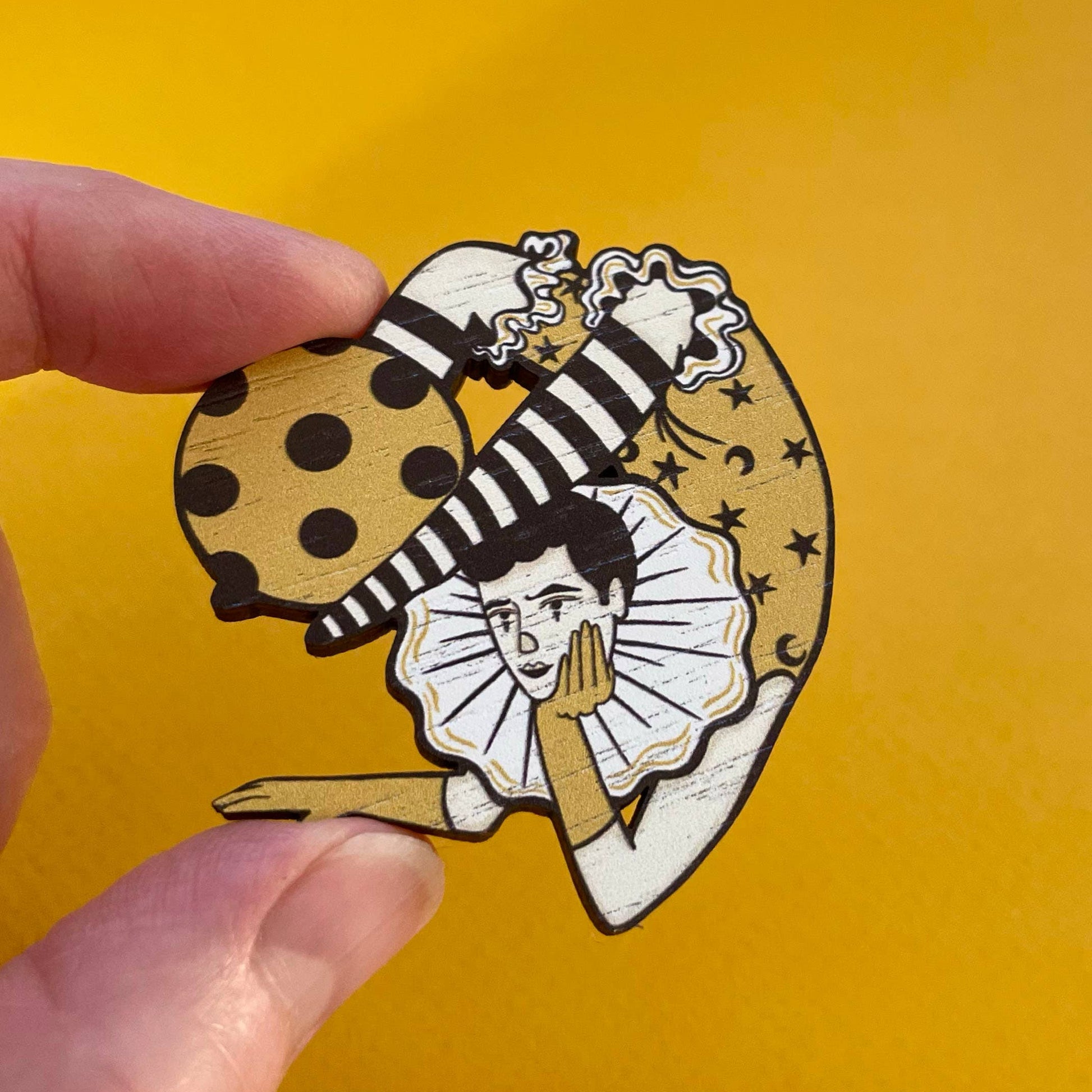 Hand holding wooden pin with circus act design on a yellow background