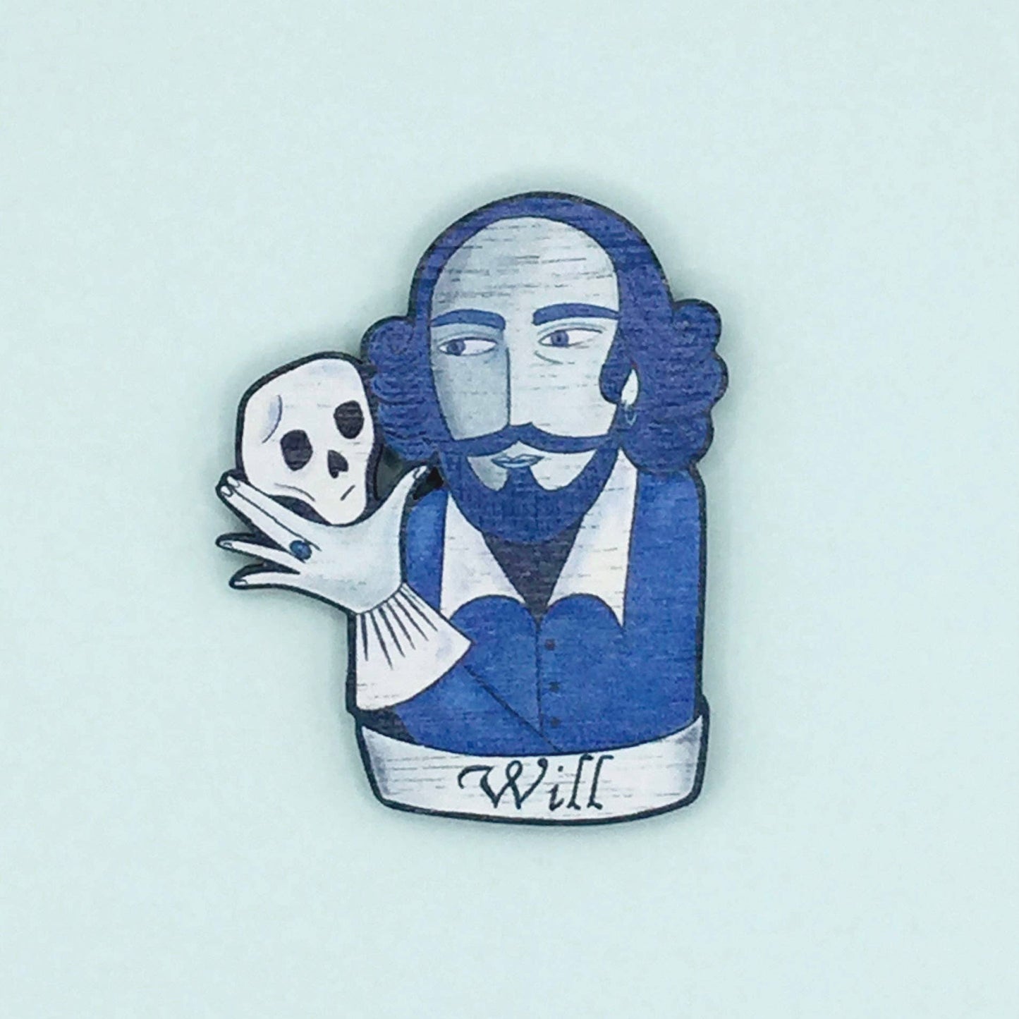 A wooden pin badge featuring William Shakespeare holding a skull