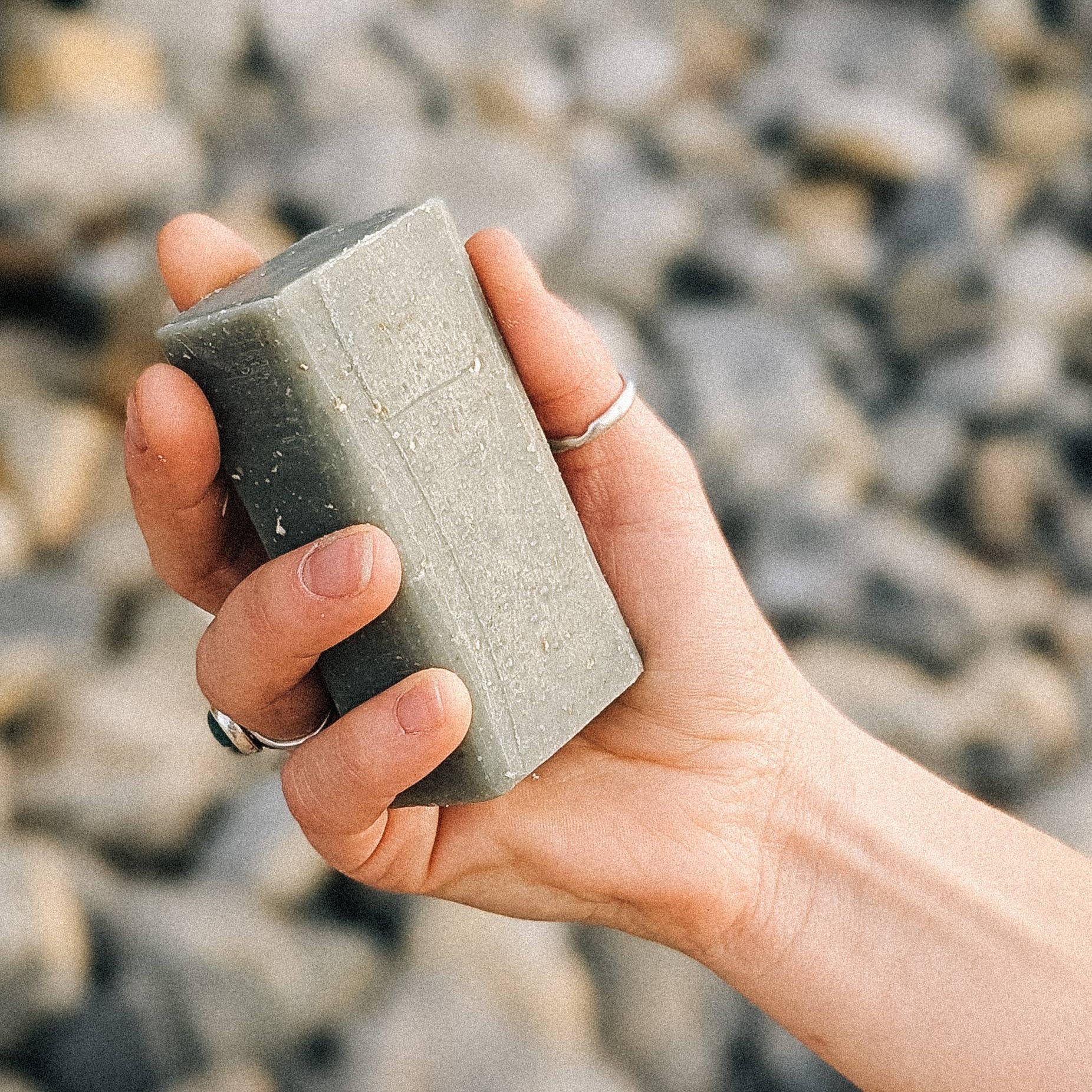 Hand holding grey bar soap against a blurred rock background