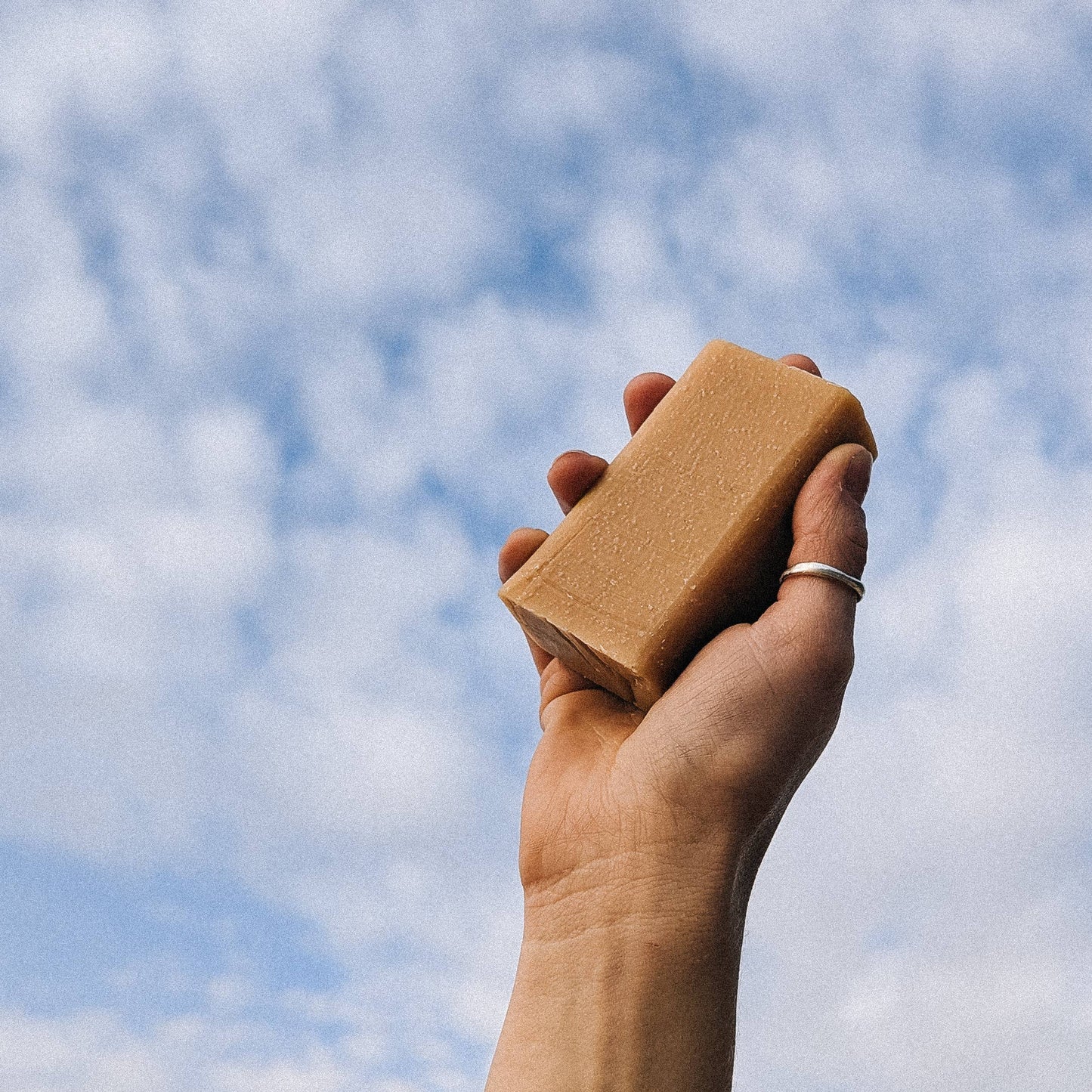 Hand holding bar of soap to the sky on a cloudy day