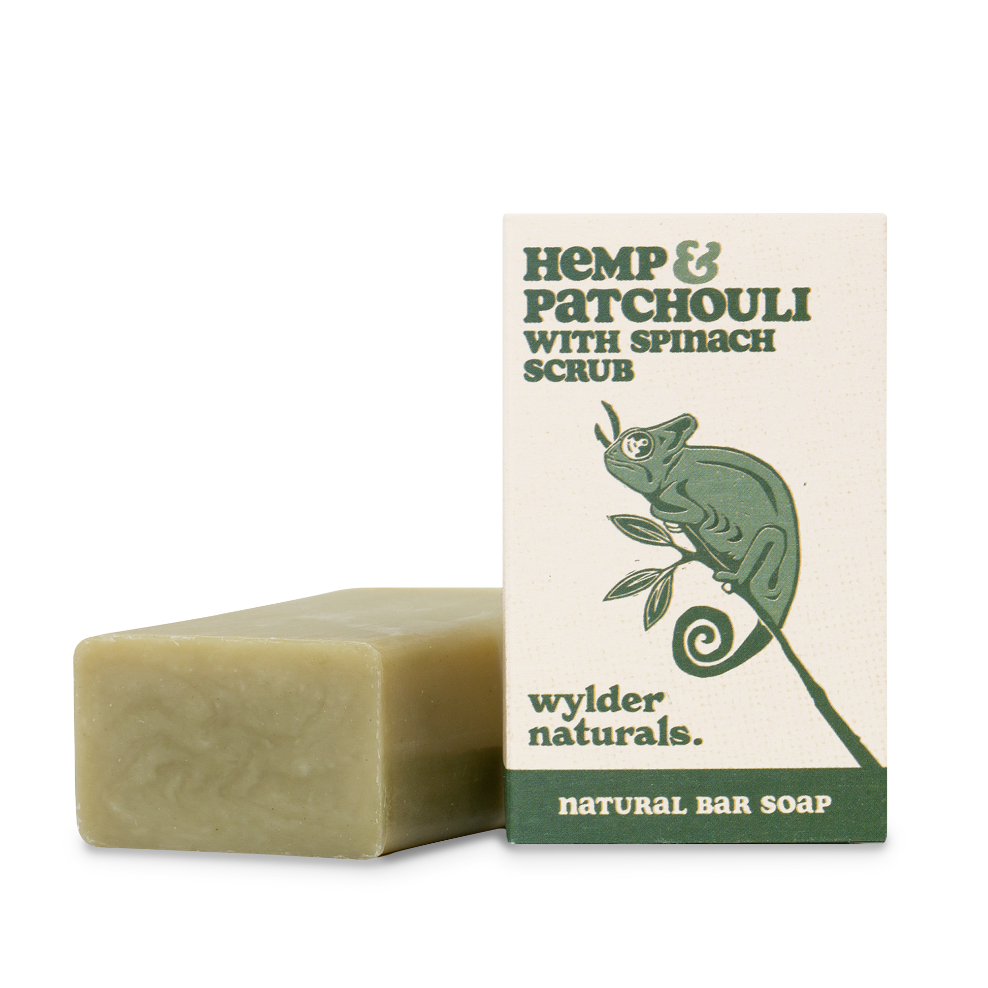 A bar of natural soap with a greenish hue, next to its packaging which features a green chameleon and text detailing the product as 'Hemp & Patchouli with Spinach Scrub'. The brand is 'Wylder Naturals' and the type as 'Natural Bar Soap'.
