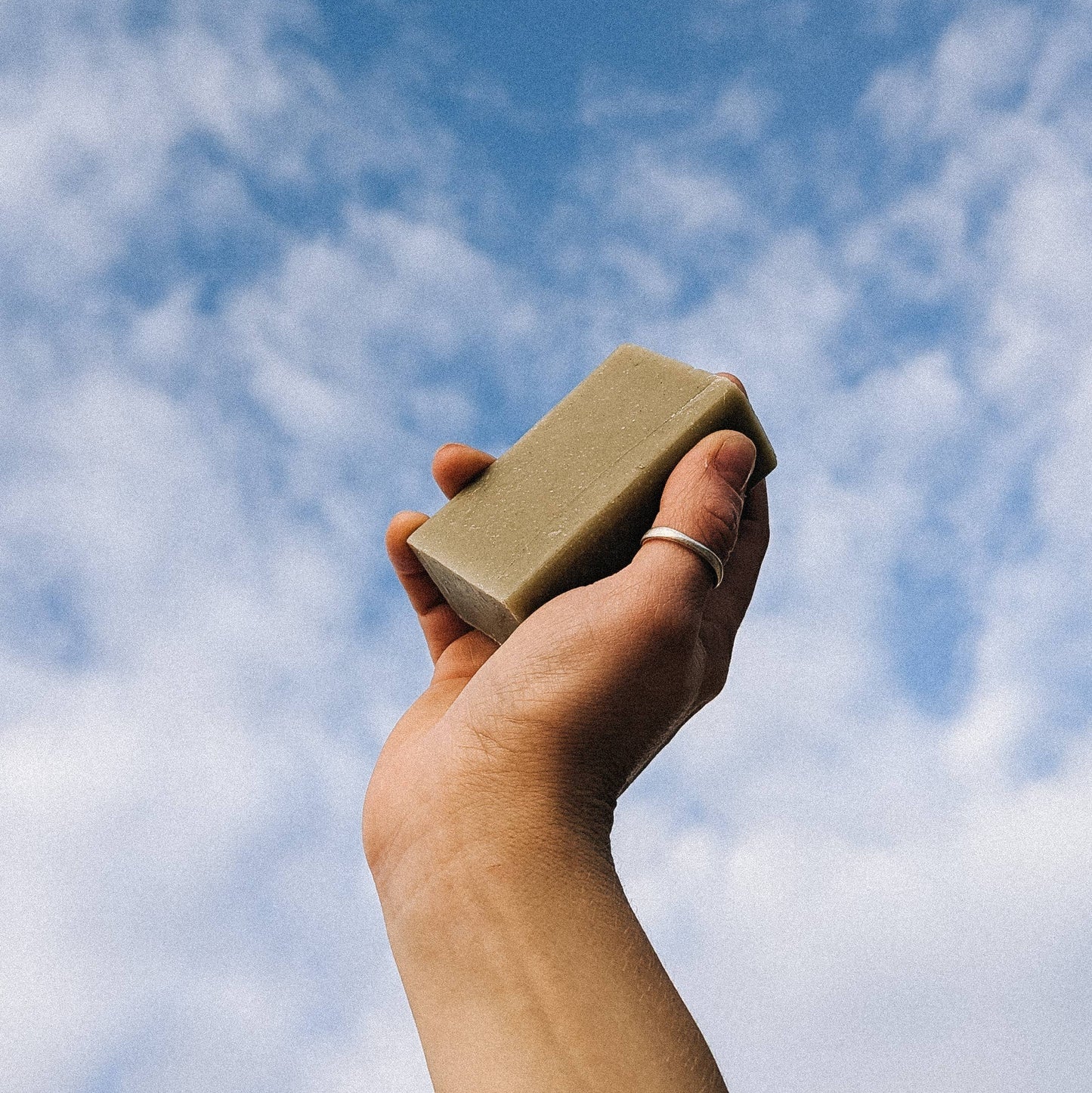 Hand holding bar soap up to the sky on a cloudy day 